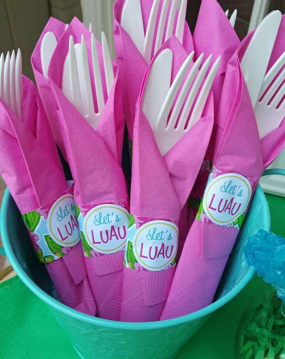 a blue bowl filled with pink plastic utensils and napkins that say let's luau