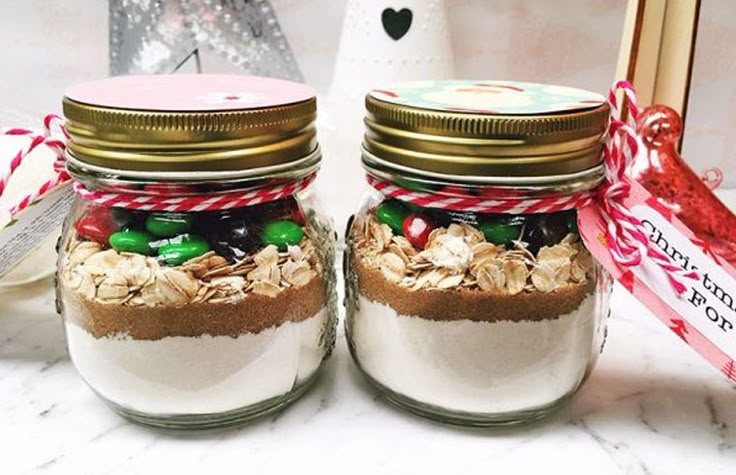 two jars filled with candy and cookies on top of a white marble counter next to a christmas decoration