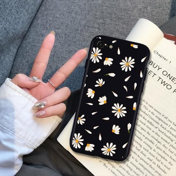 a woman holding up her phone case with daisies on it