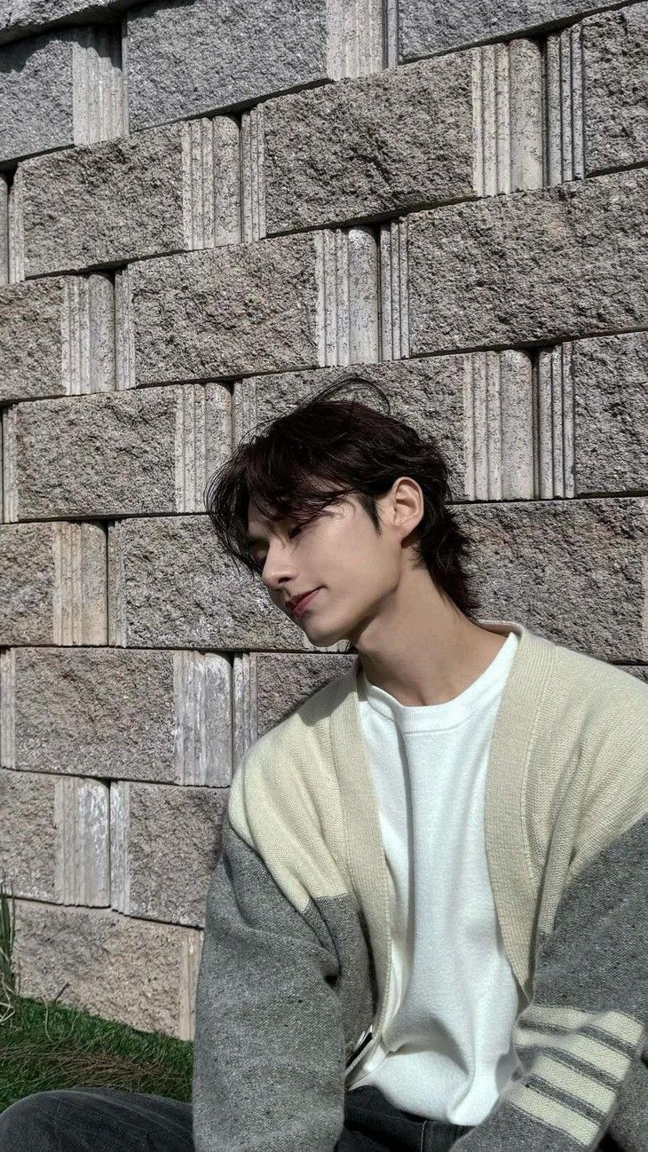 a young man sitting on the ground in front of a brick wall