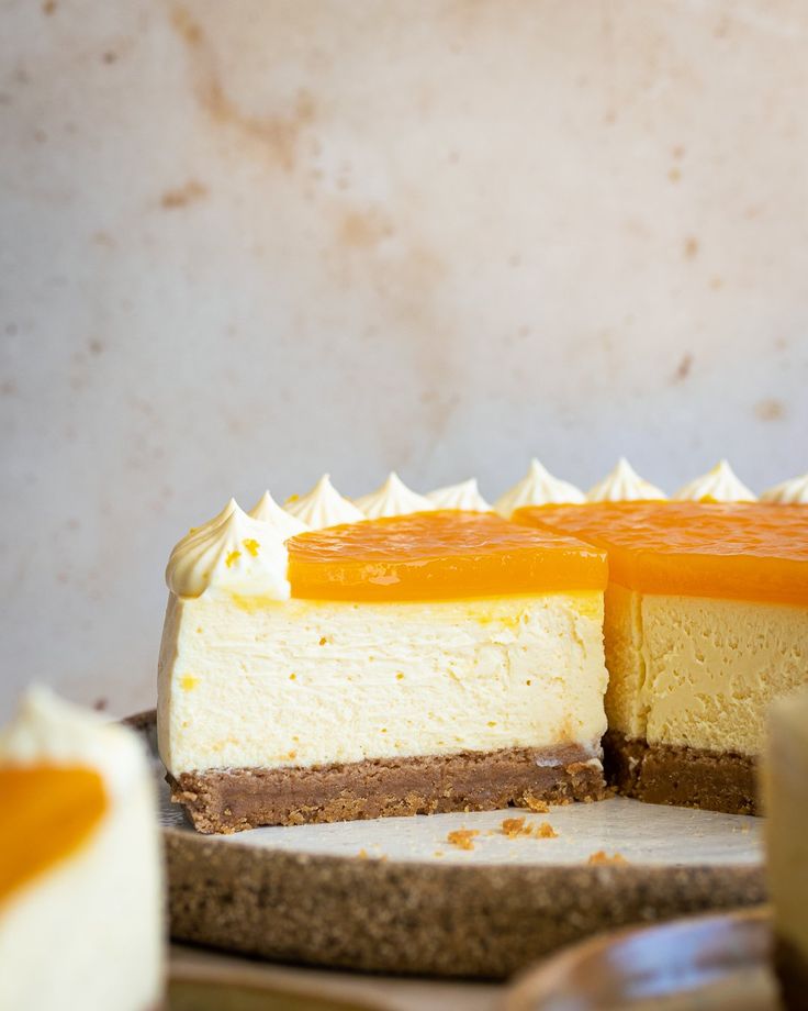 a cheesecake with an orange topping is on a wooden cutting board next to other desserts