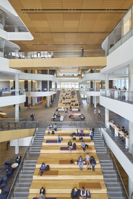 people are sitting at tables in the middle of a large building with stairs and balconies