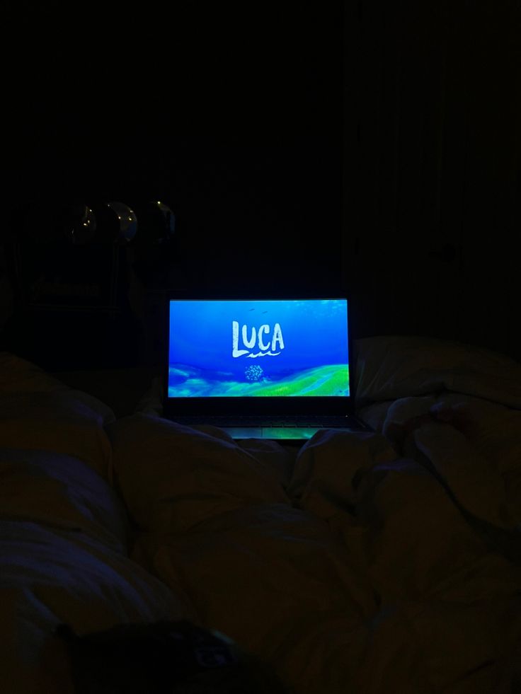 an open laptop computer sitting on top of a bed in the dark with luca written on it