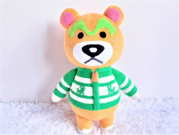 a teddy bear wearing a green and white striped sweater on top of a pile of snow