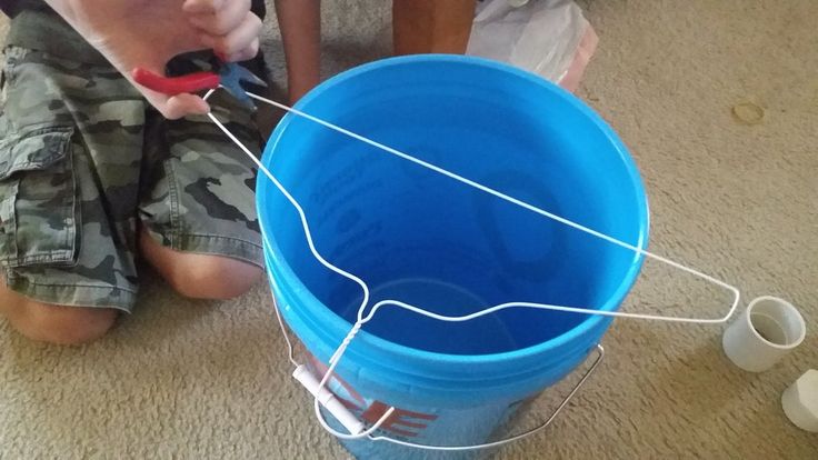 a young boy sitting on the floor next to a blue bucket filled with water and toothbrushes