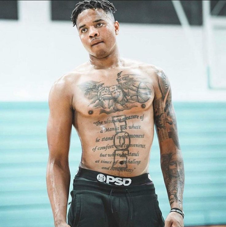 a man with tattoos on his chest standing in front of a basketball court and looking at the camera