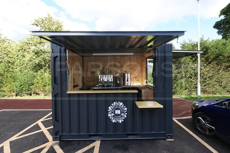 a starbucks coffee stand in a parking lot next to a blue sports car and trees