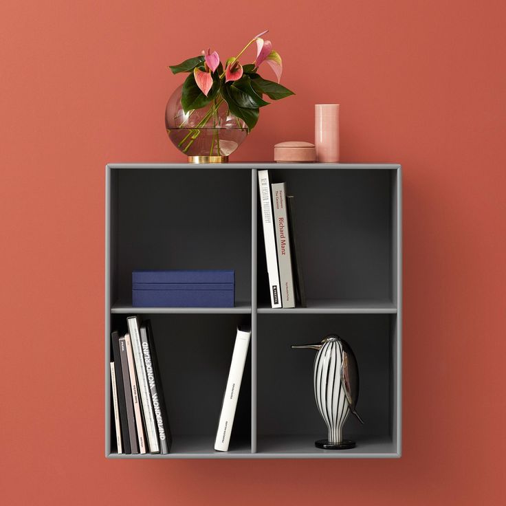 a shelf with some books and a vase on it next to a wall painted pink