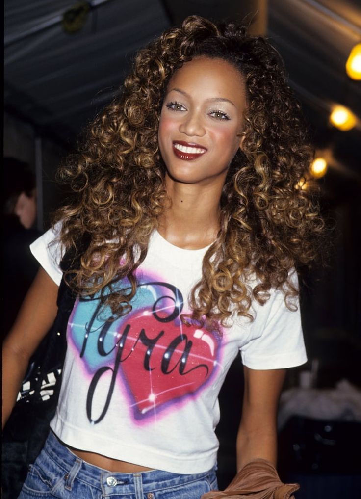 a woman with curly hair wearing a t - shirt and denim shorts holding a purse