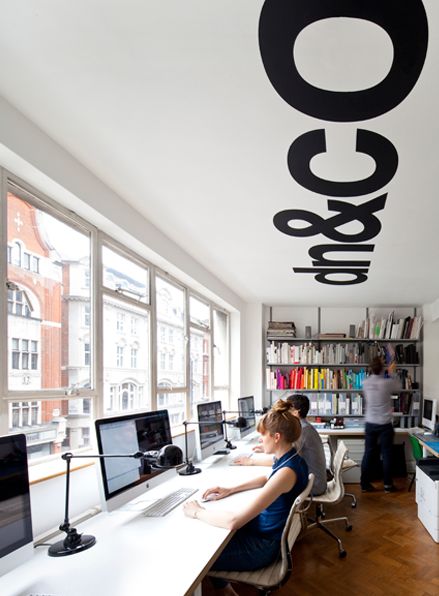 two people sitting at desks in an office with large windows and bookshelves