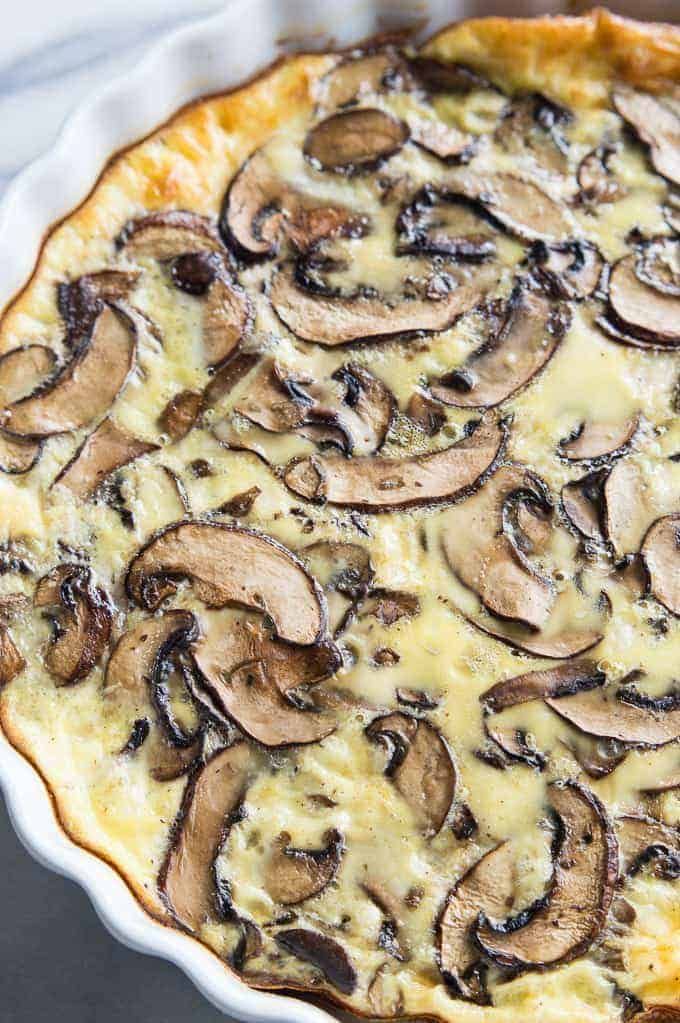 a quiche with cheese and mushrooms in a white dish on a marble countertop