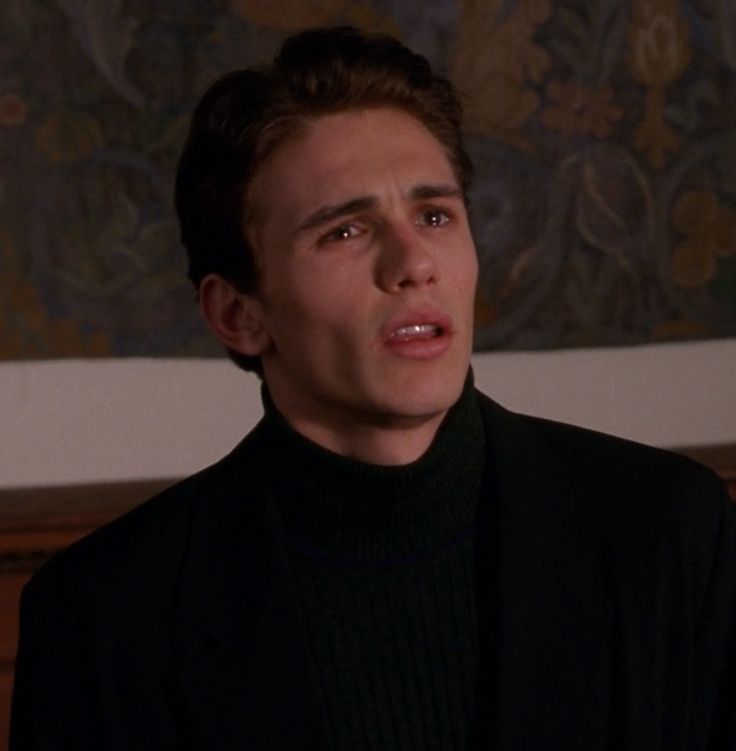 a young man in a black turtle neck sweater looks at the camera and stares into the distance