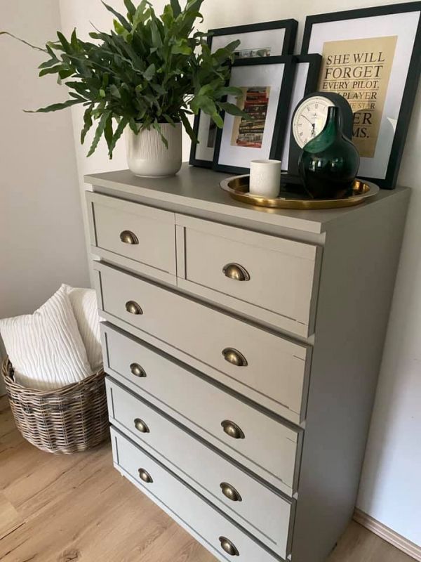 a white dresser with some pictures on it and a potted plant next to it