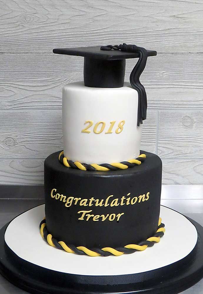 a graduation cake that is decorated with black and white frosting, gold lettering and a graduate's cap on top