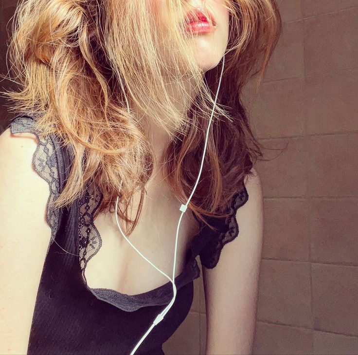 a woman with long hair wearing headphones and looking off to the side, in front of a brick wall