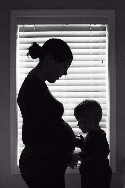 a woman standing next to a child in front of a window with blinds on it