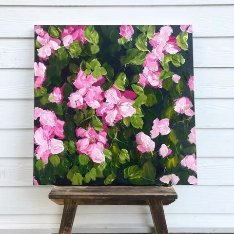 a painting of pink flowers sitting on top of a wooden easel in front of a white house