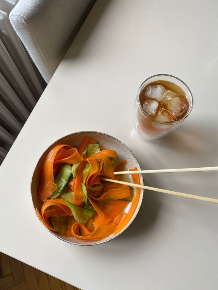 a bowl of food with chopsticks next to it and a drink on the table