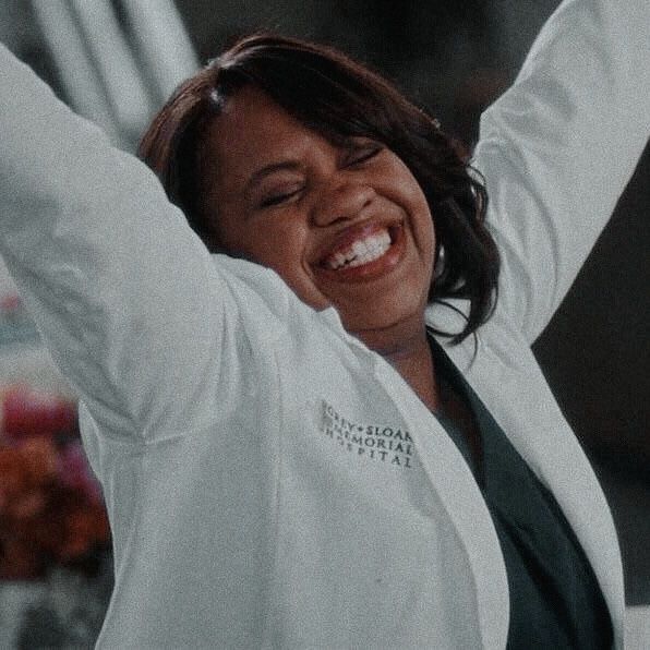 a woman in a lab coat holding her arms up to the side and smiling with both hands behind her head