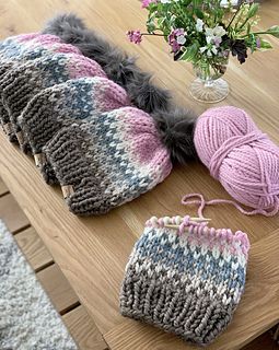 knitted hats and mittens sitting on a table next to a vase with flowers