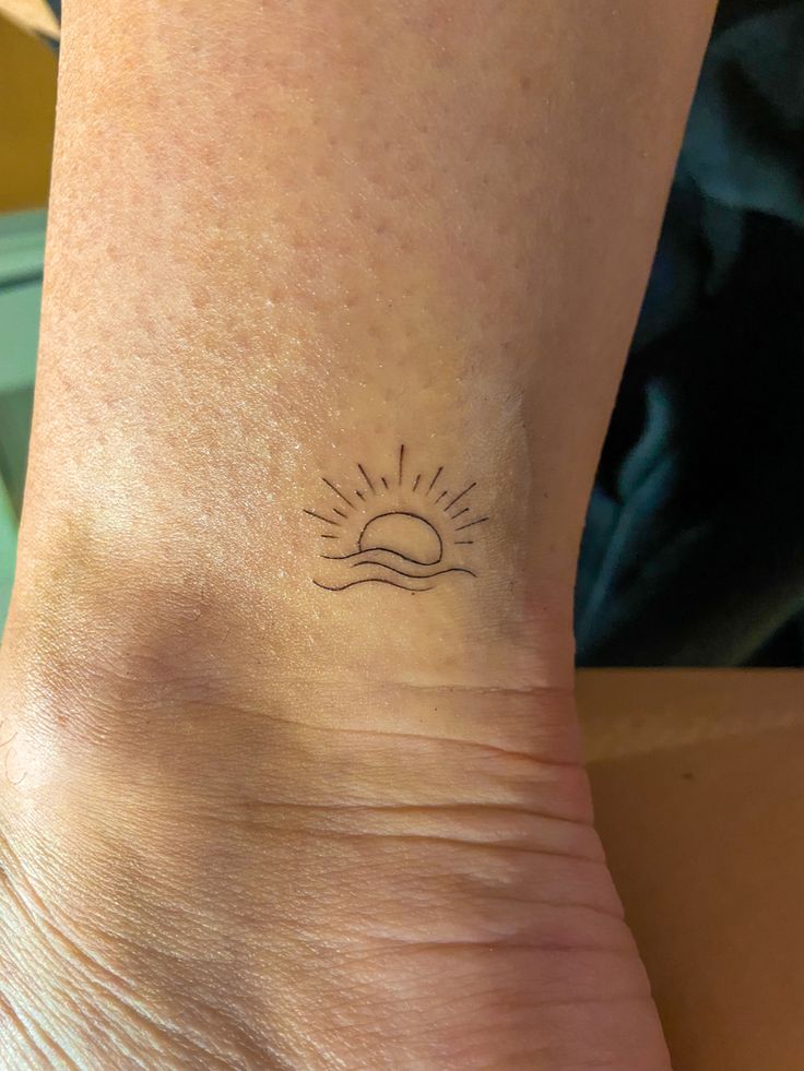 a person with a small tattoo on their left foot and the sun above them is shining