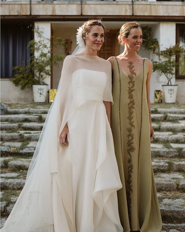 two women standing next to each other in front of a building wearing dresses and veils