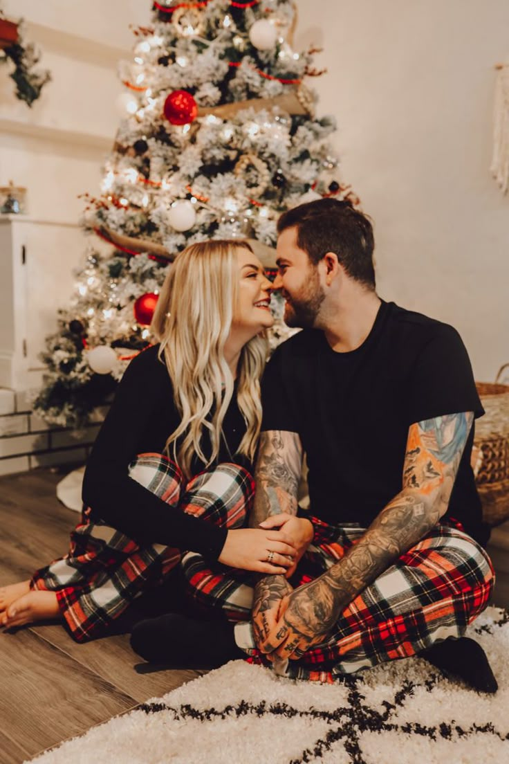 a man and woman sitting in front of a christmas tree with their arms around each other