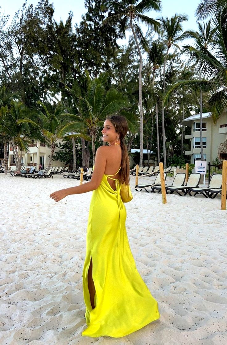 a woman in a yellow dress is walking on the beach with palm trees behind her