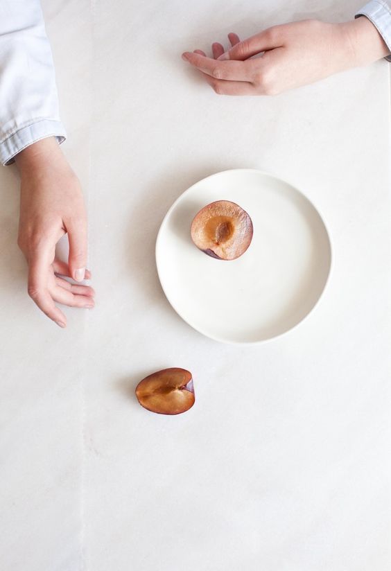 two hands reaching for an uncooked donut on a white plate next to another person's hand