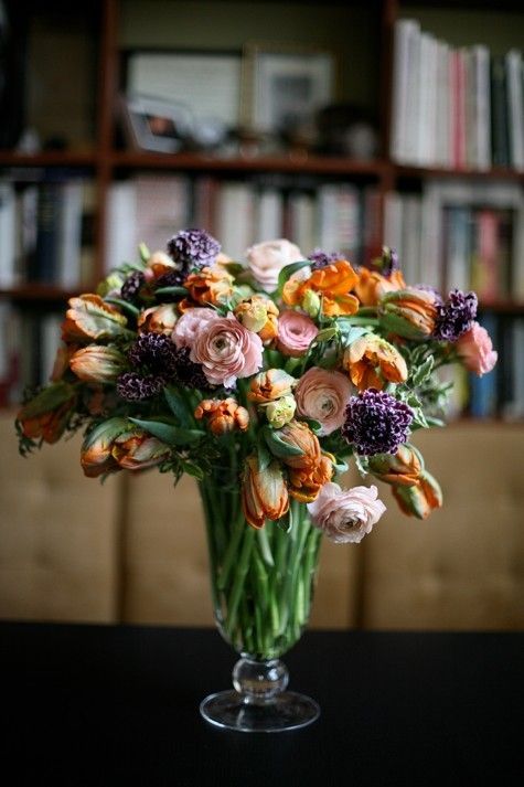 a vase filled with lots of flowers sitting on top of a table next to a book shelf