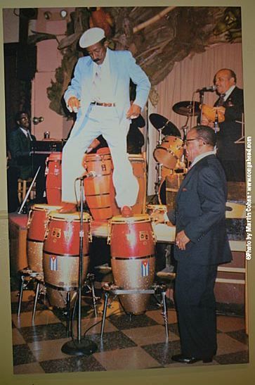 two men standing next to each other in front of drums