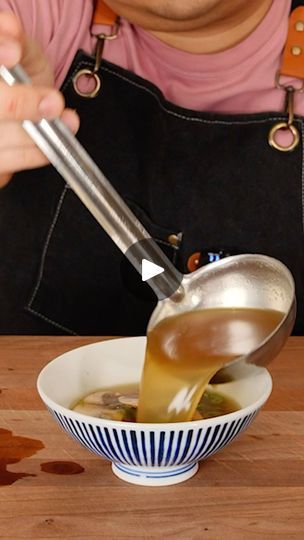 a person pouring liquid into a bowl with a ladle in it on top of a wooden table