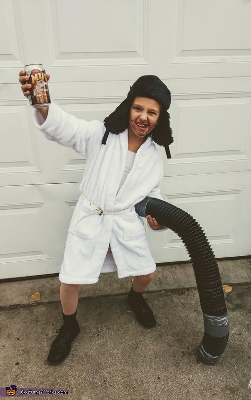 a young boy dressed as jesus holding a can of beer and wearing a robe while standing in front of a garage door