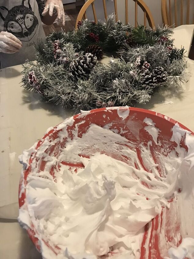 a red bowl filled with whipped cream sitting on top of a table next to a wreath