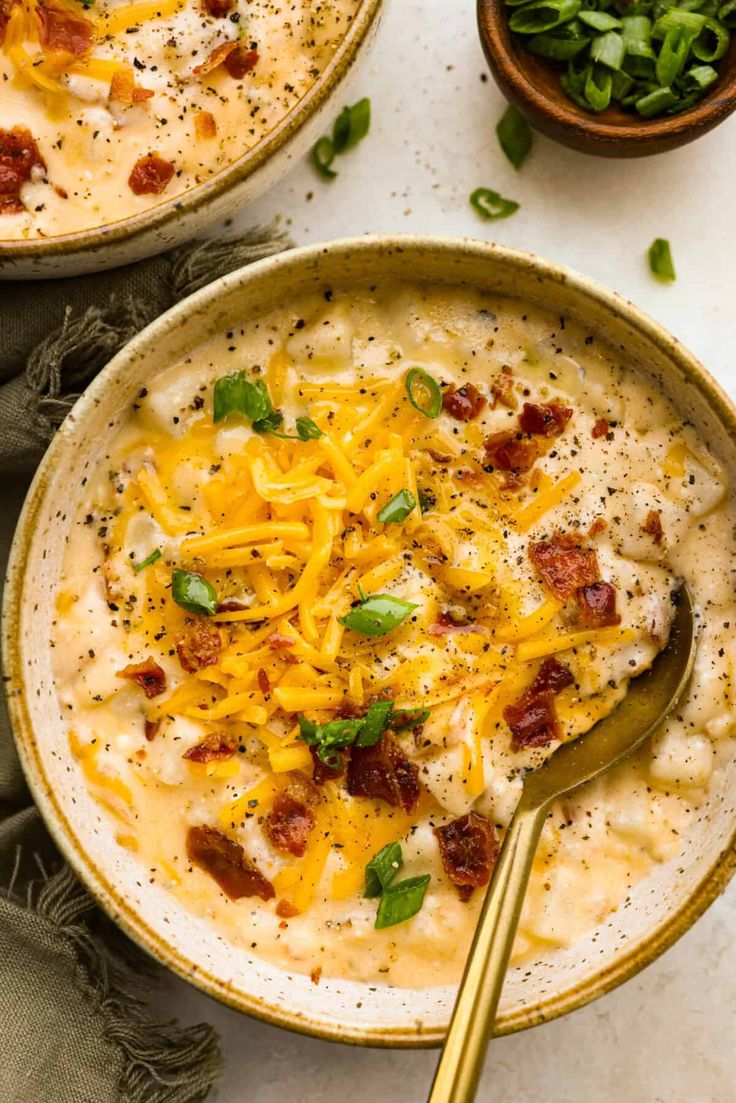 two bowls of soup with cheese and bacon on top, one has a spoon in it