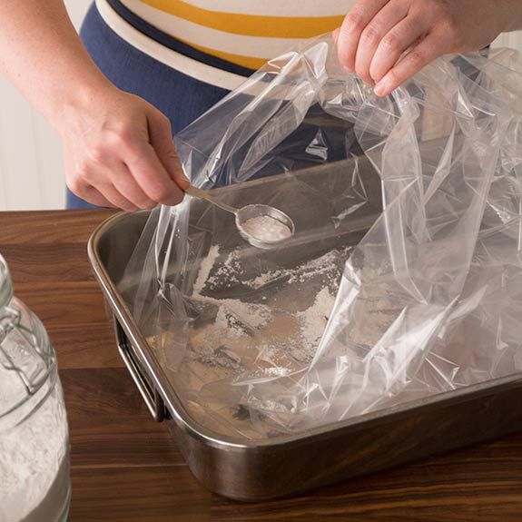 a person is unpacking some food in a metal pan on a wooden table