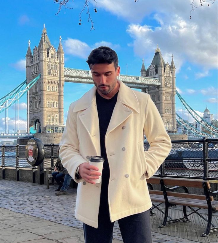 a man standing in front of a bridge holding a drink and looking at the camera