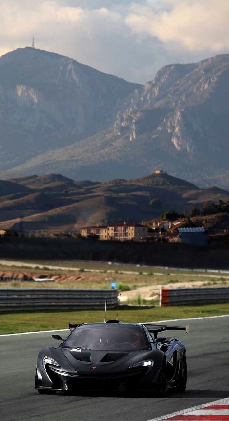 a black sports car driving on a race track with mountains in the background