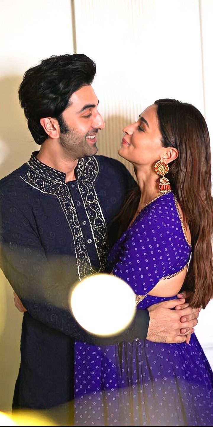 a man and woman standing next to each other in front of a white wall with their arms around each other