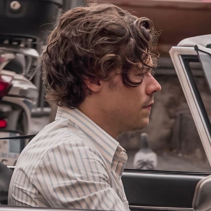 a young man sitting in the driver's seat of a car looking off into the distance