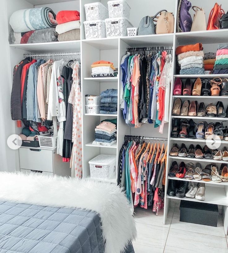 an organized closet with clothes, shoes and other items on shelving unit shelves in front of bed