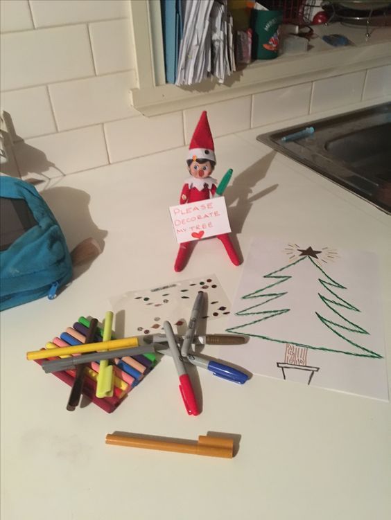 an elf is sitting on top of the kitchen counter with crayons and pencils