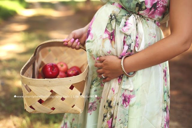 a pregnant woman holding a basket full of apples