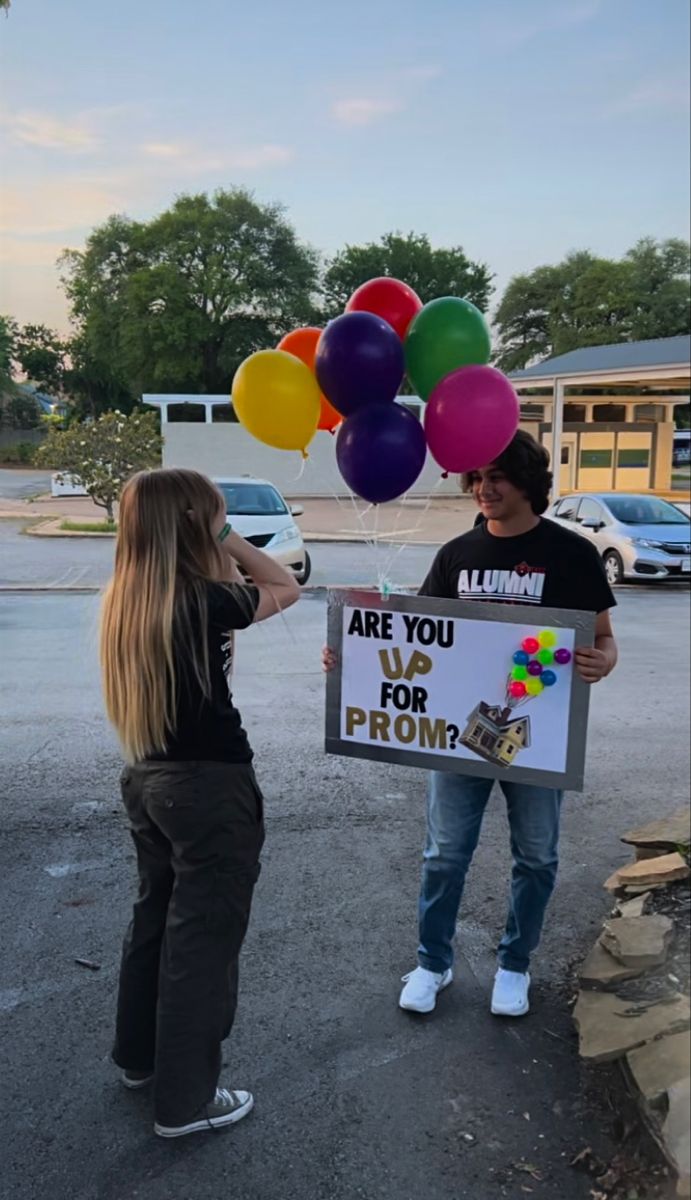 a man holding a sign with balloons attached to it while standing next to a woman