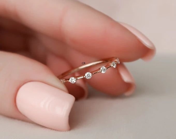 a woman's hand holding a gold ring with three small white diamonds on it