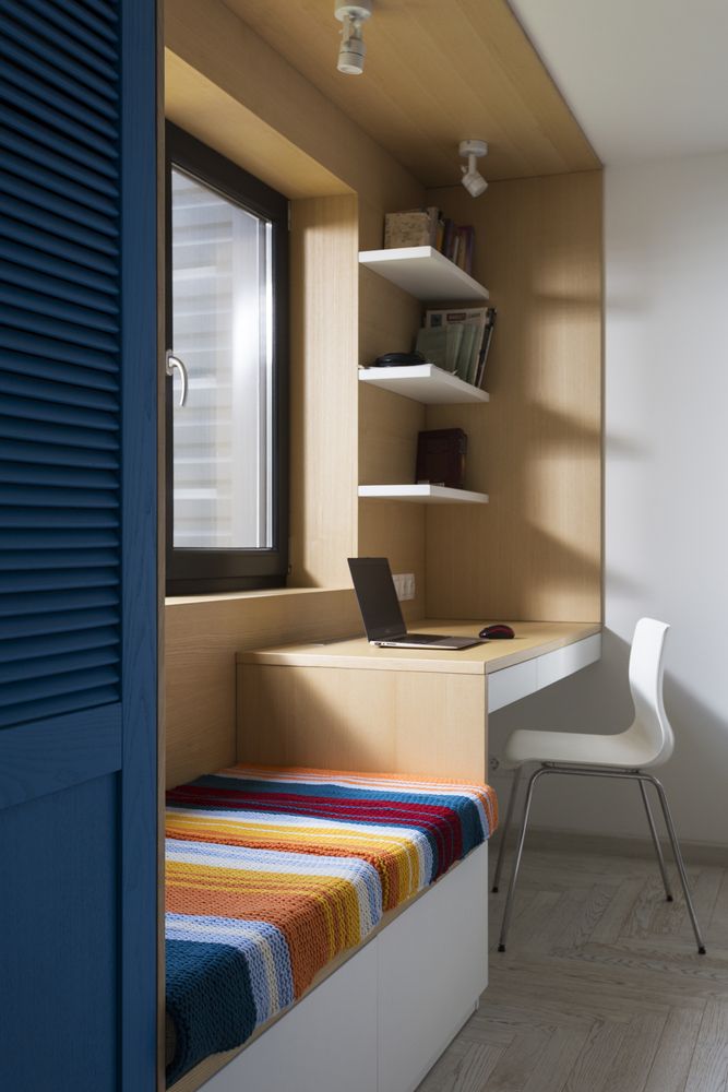 a room with a bed, desk and chair next to a wall mounted book shelf