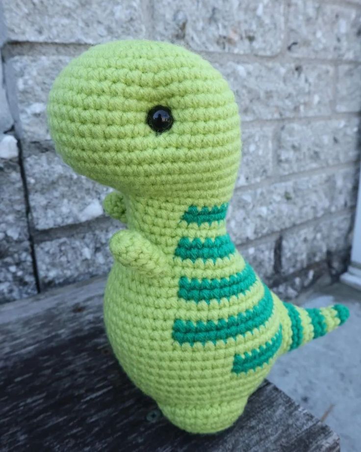 a crocheted stuffed toy sitting on top of a wooden bench next to a brick wall