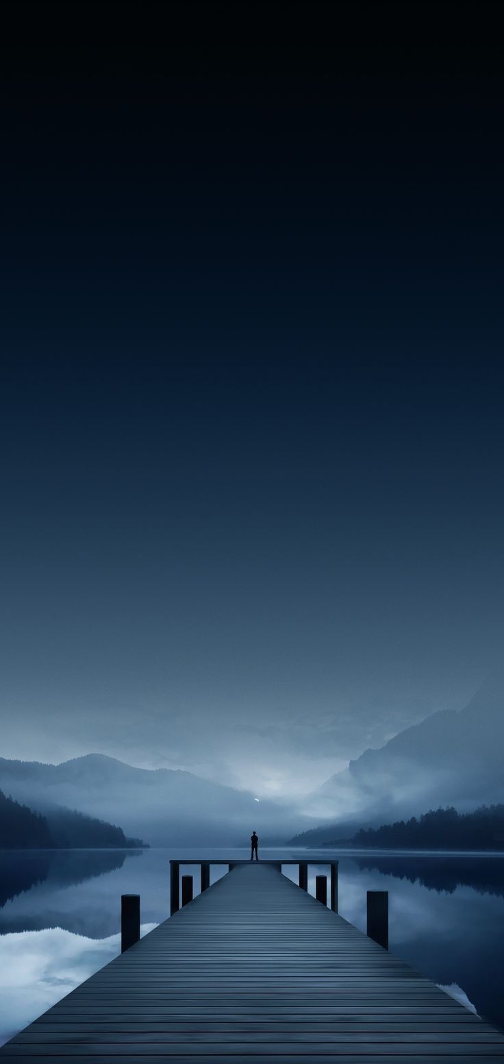 a person standing on a dock in the middle of a body of water at night