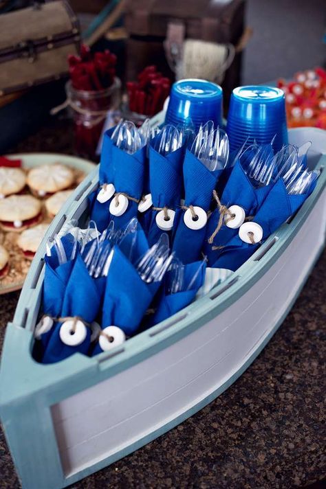 there are many blue cups in the boat on the table with cookies and other food