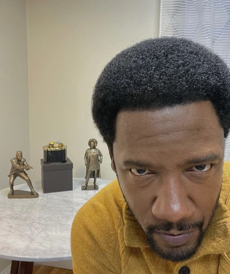 a man with an afro looks at the camera while sitting in front of a table